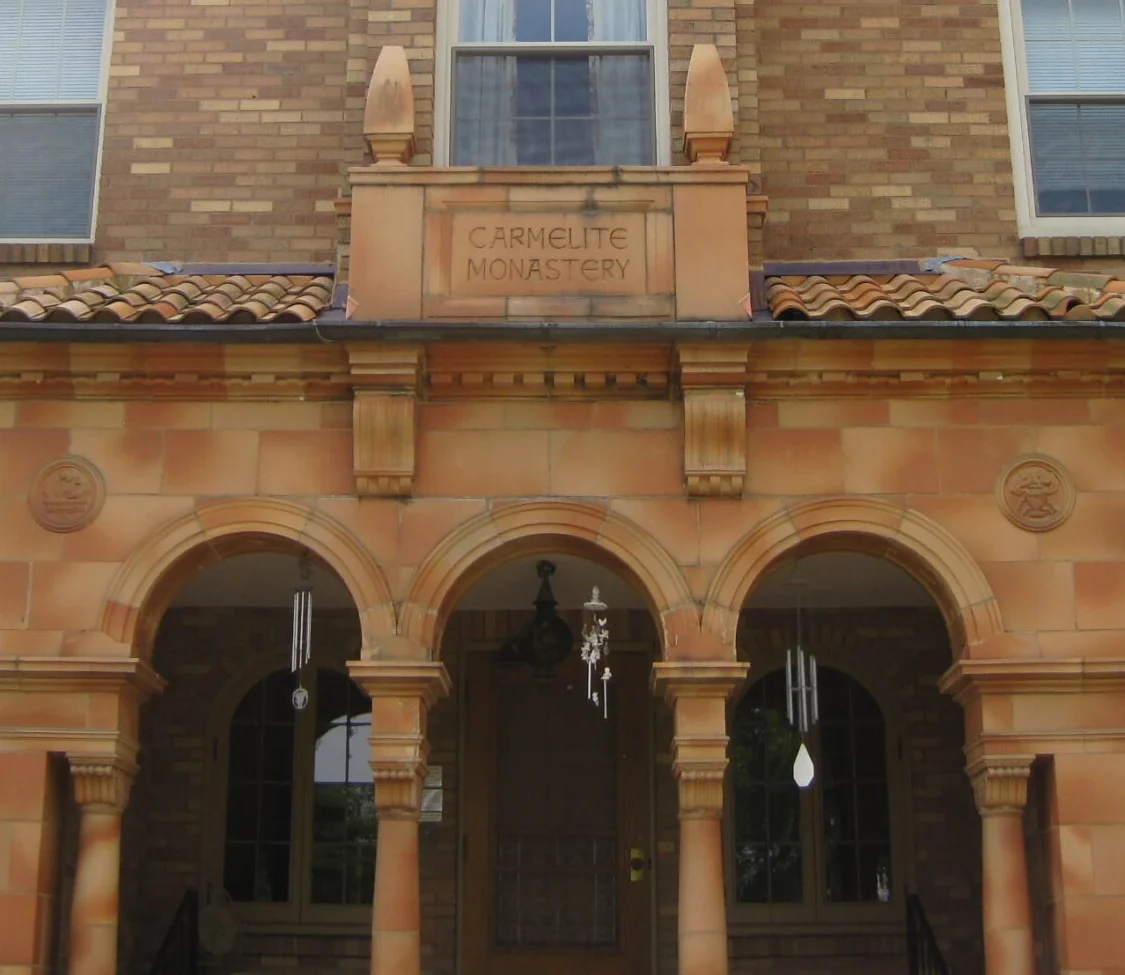 A brick building with arched entrances and decorative details marked "Carmelite Monastery." The facade is warm-toned with a serene, historical feel.