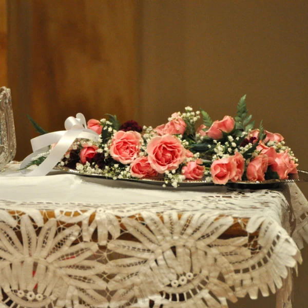 A delicate floral arrangement of pink roses and green foliage on a lace-covered table, exuding elegance and romance. Floral sketches adorn the corner.